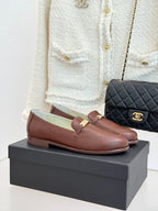 Women’s brown leather loafers with gold buckle detail, on a black shoe box