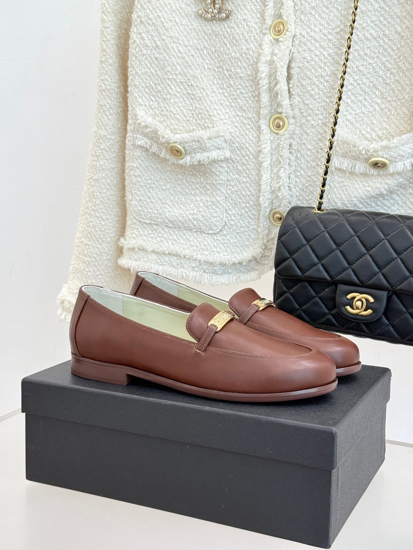 Women’s brown leather loafers with gold buckle detail, on a black shoe box