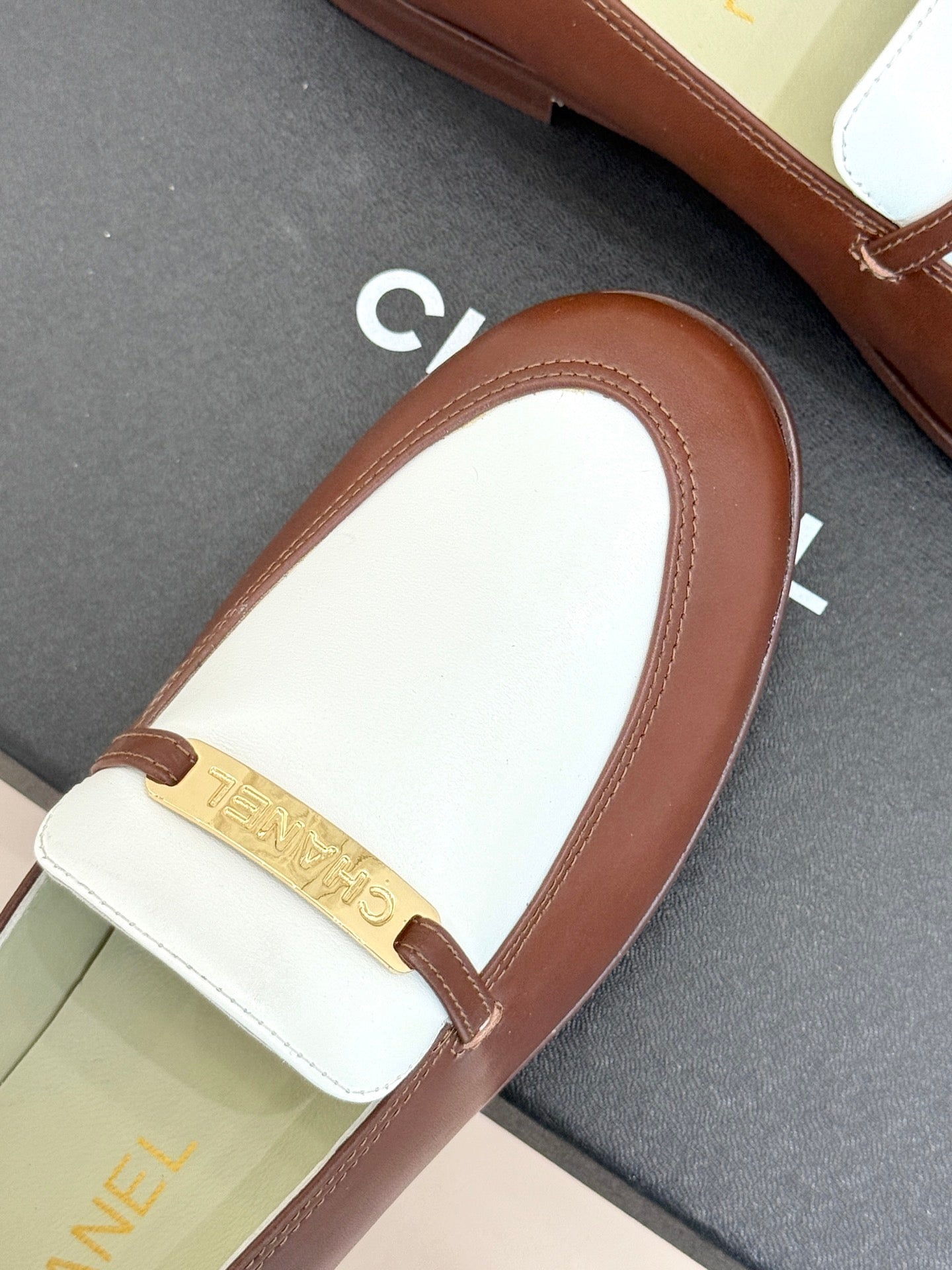 Chanel ladies luxury loafer close-up, brown leather toe with white strap and gold bar