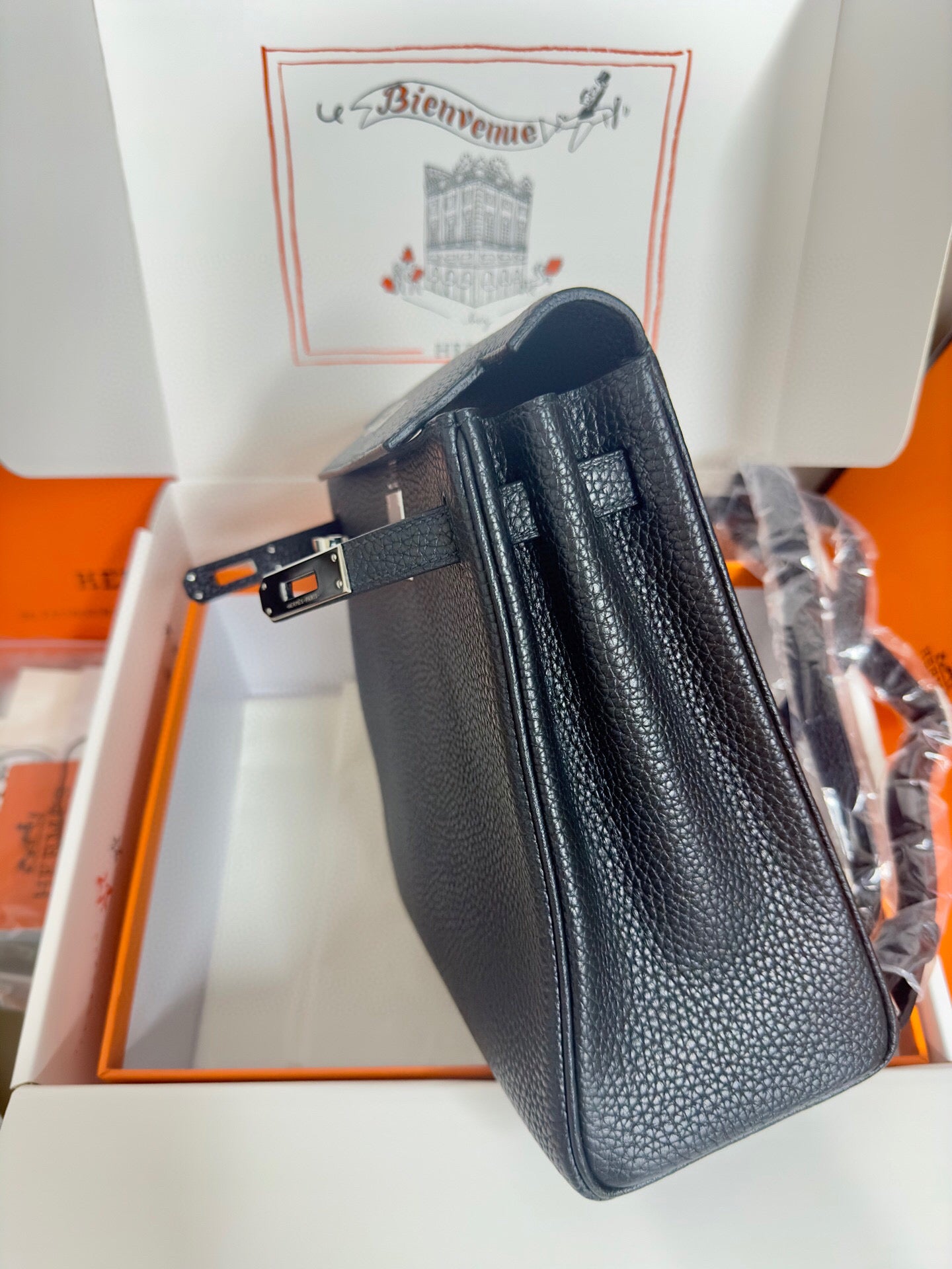 Hermes handbag side view in dark textured leather with top handle and belt strap.