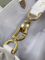Dior bag close-up of gold tone strap hardware and D-ring clasp on light white leather