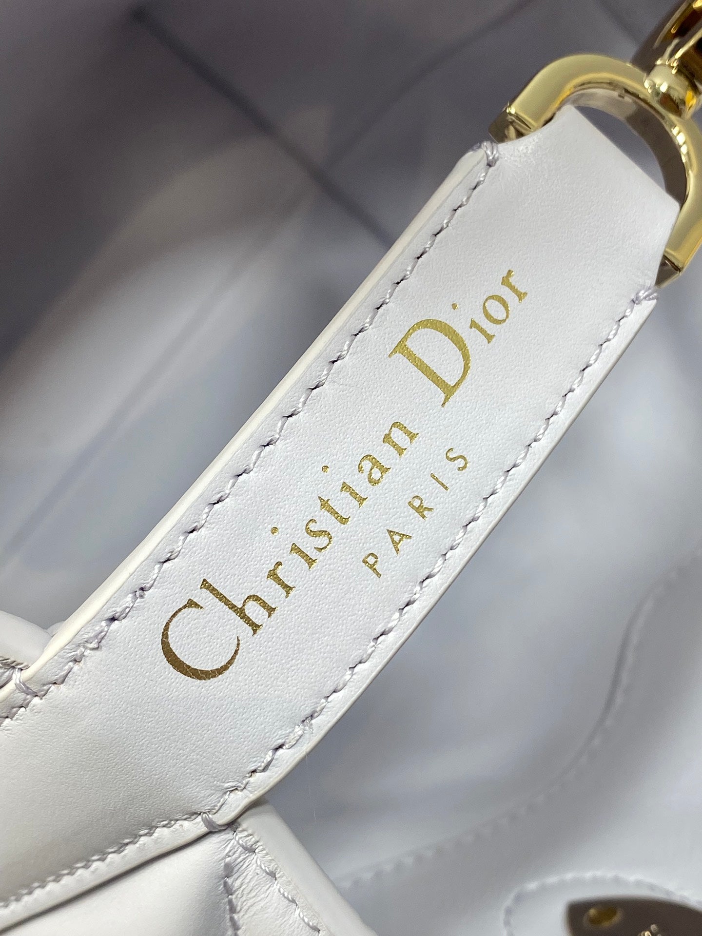 Dior bag strap close-up with stitched "Christian Dior" text on light white leather