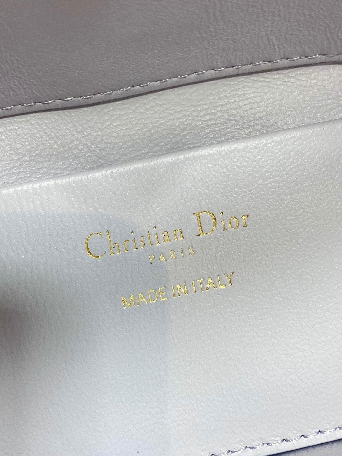 Dior bag close-up of "Christian Dior" and "MADE IN ITALY" stamping on light white leather
