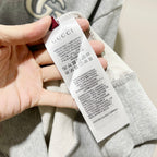 Gucci long-sleeve hoodie care label tag held by hand, heather gray inside neck area