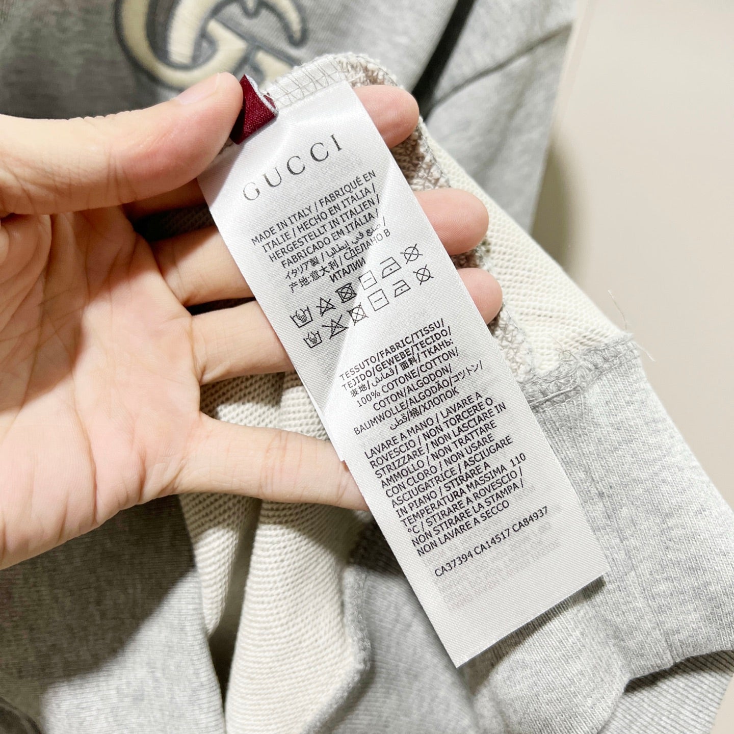 Gucci long-sleeve hoodie care label tag held by hand, heather gray inside neck area