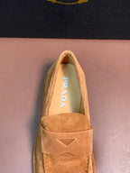 Prada tan suede loafer close-up with triangular emblem and PRADA on insole.