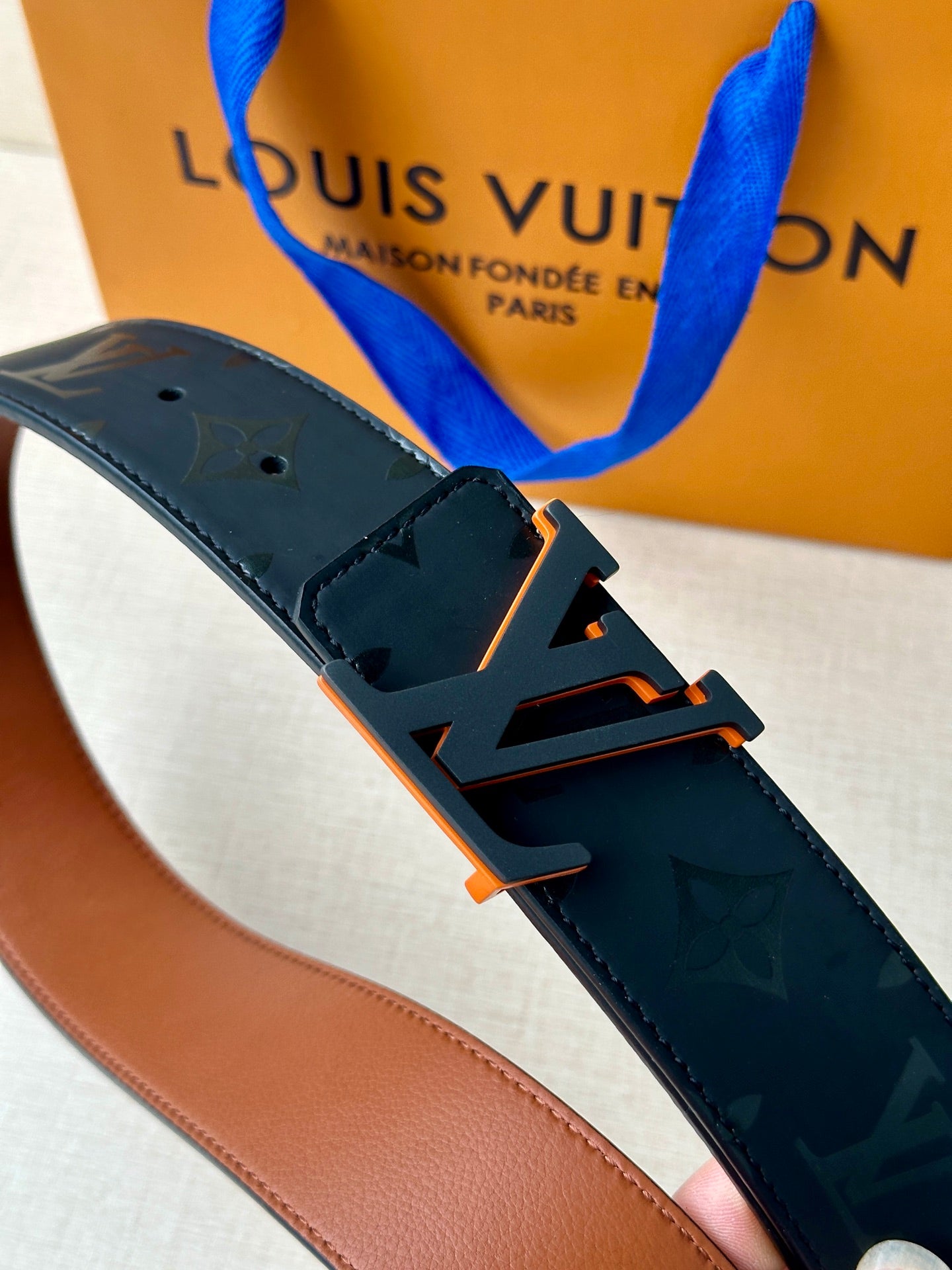 Louis Vuitton belt: dark blue monogram strap with orange-toned buckle hardware.
