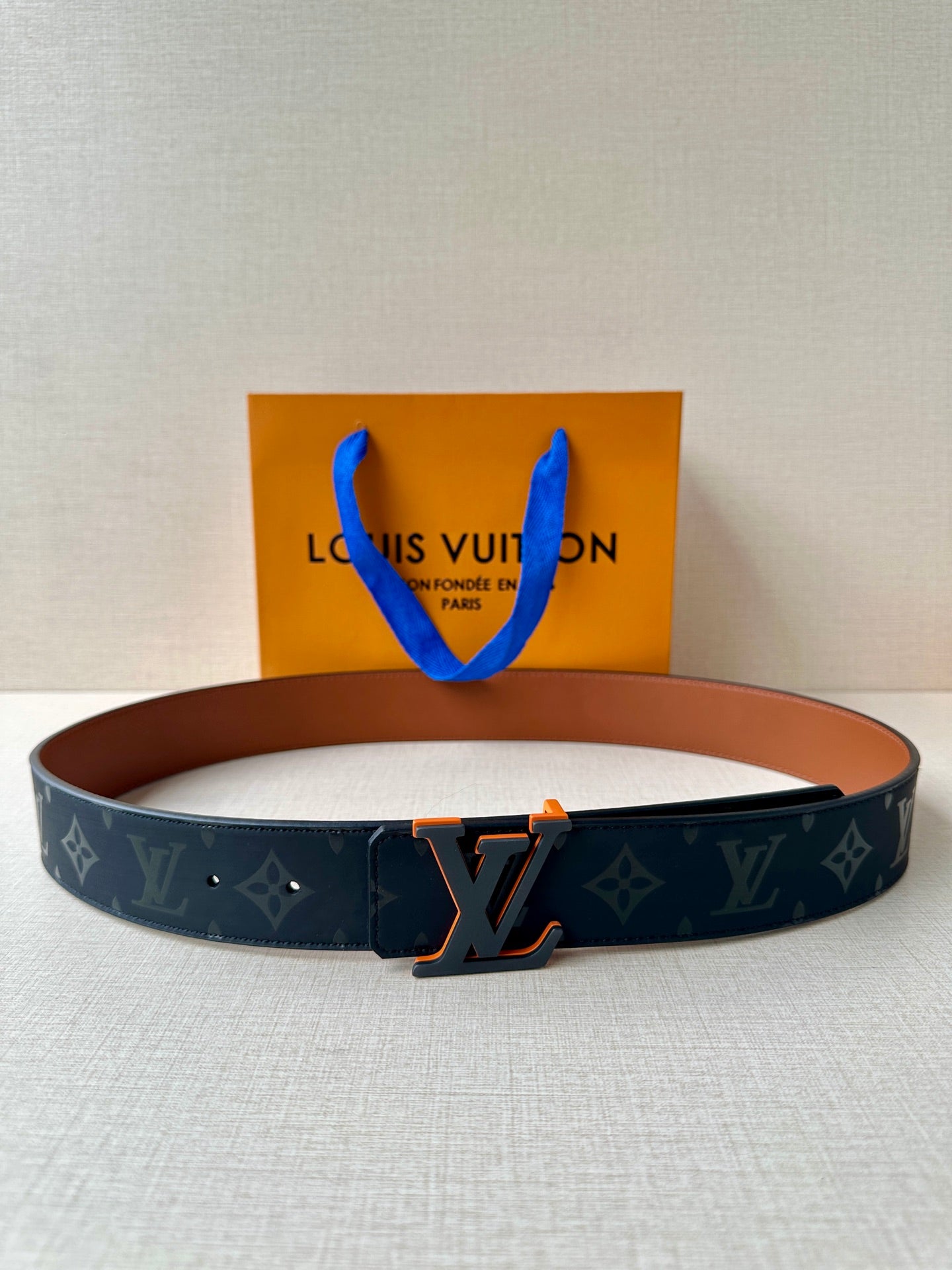 Louis Vuitton belt: dark blue monogram strap, tan lining, metal buckle.