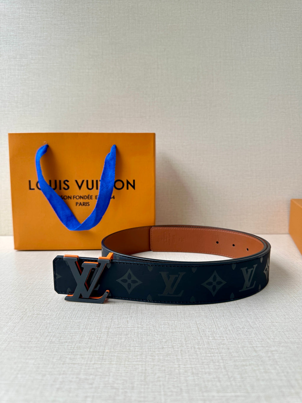 Louis Vuitton belt: dark blue monogram strap with tan backing and orange buckle.