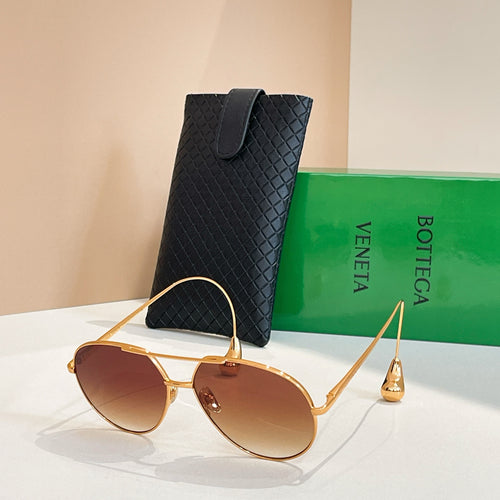 Bottega Veneta glasses with gold frame and amber lenses, next to black case