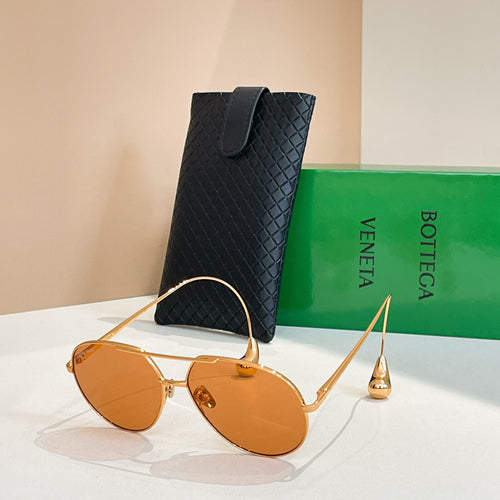 Bottega Veneta glasses with gold frame and amber-tinted lenses, beside black case