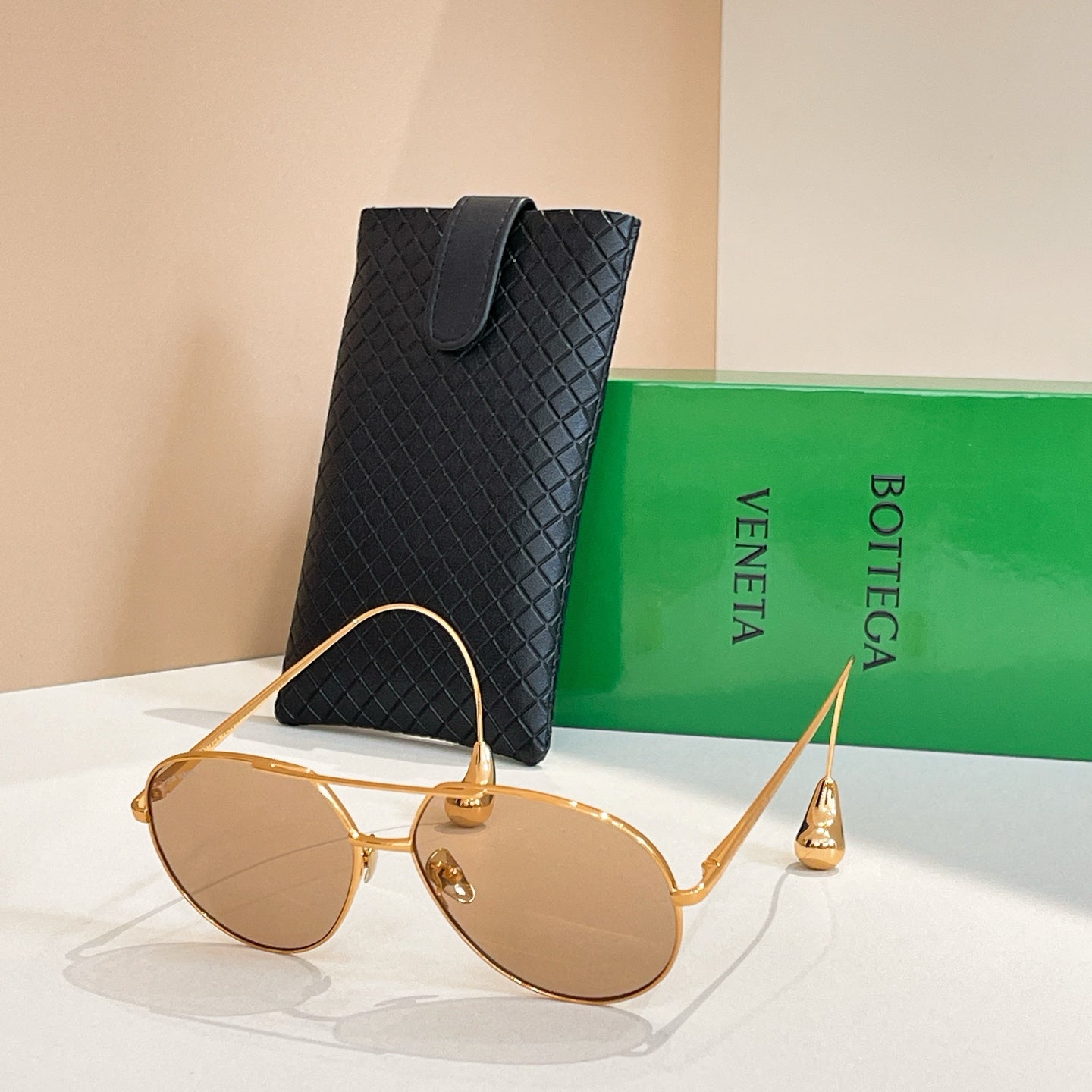 Bottega Veneta glasses with gold frame and amber lenses, front view by black case