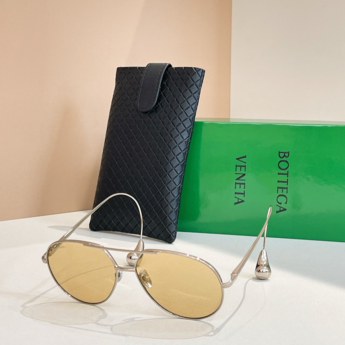 Bottega Veneta glasses with gold frame and tan lenses, beside black case