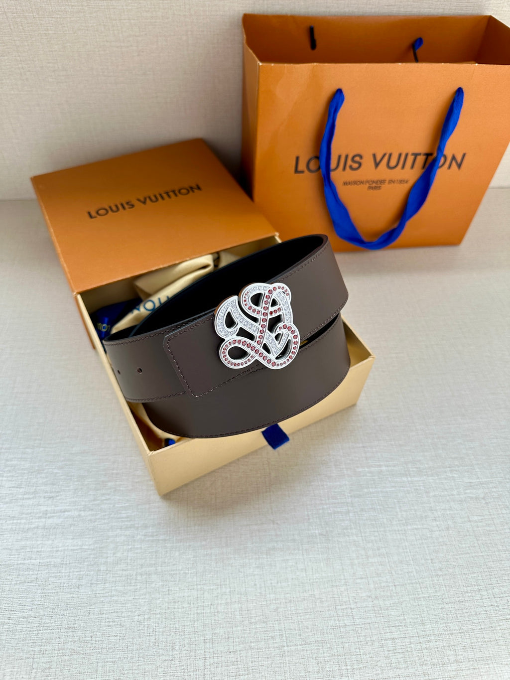 Dark navy leather belt with gem monogram buckle, shown in open gift box