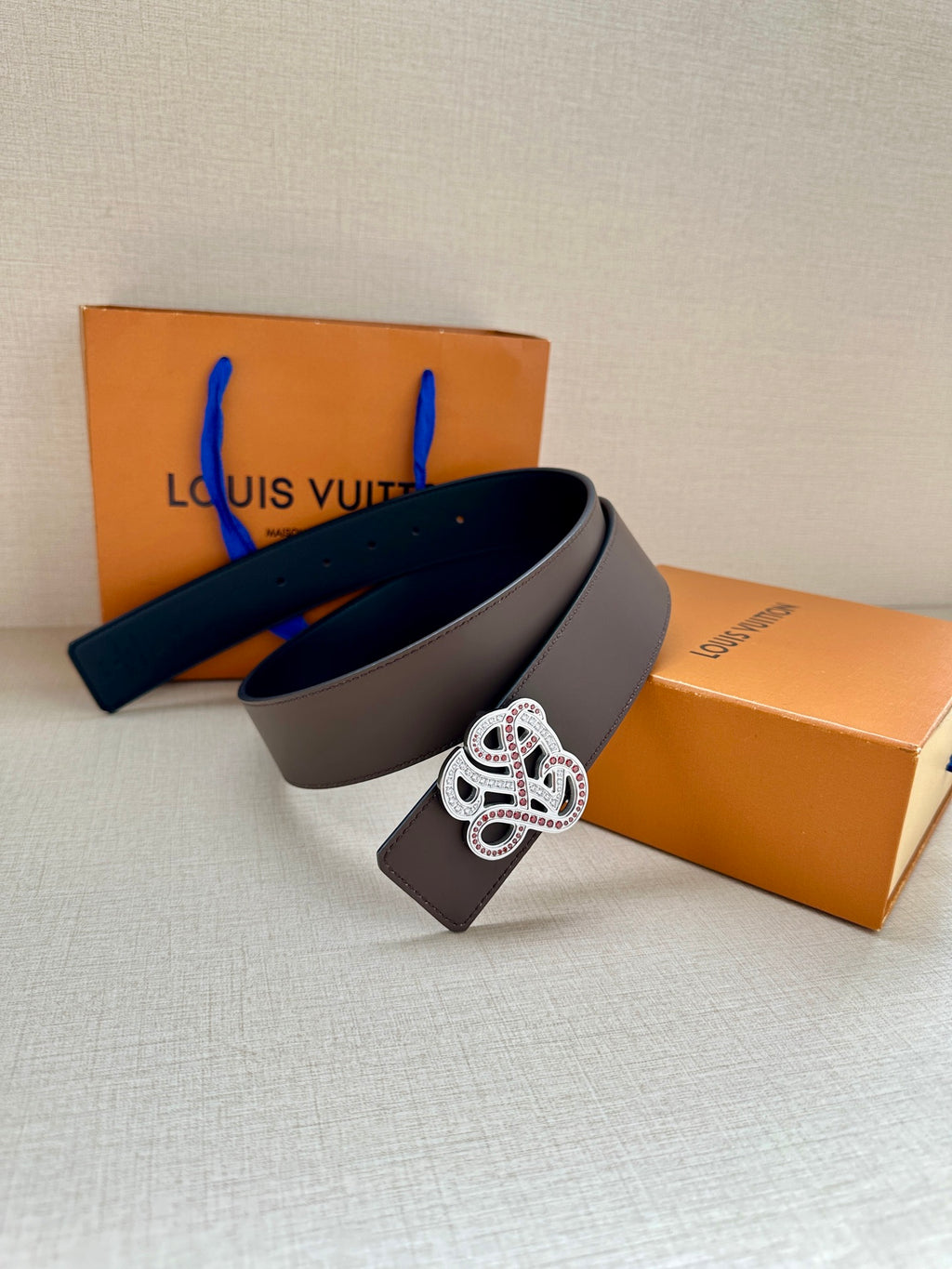 Dark navy leather belt with gold-tone monogram buckle, draped over box