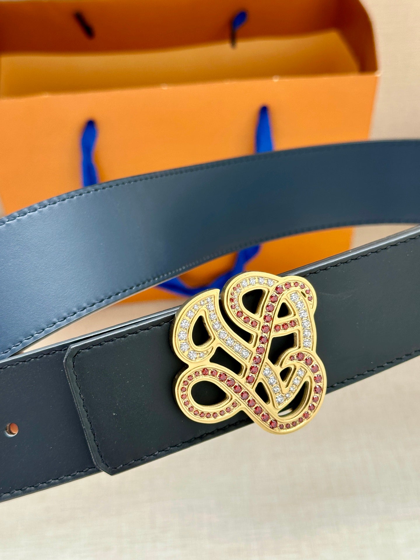 Dark blue leather belt with jeweled logo buckle close-up
