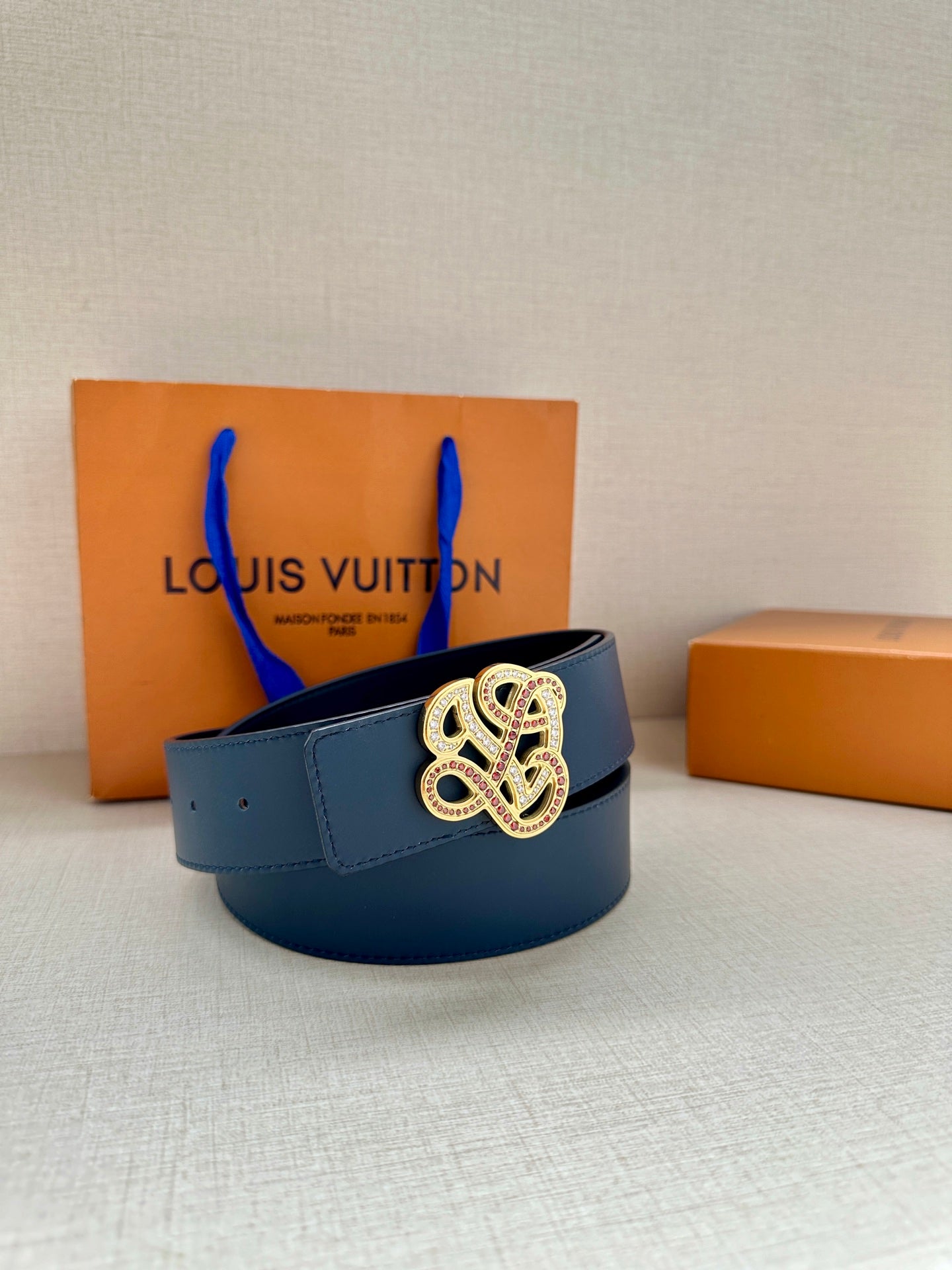 Dark blue leather belt with ornate buckle resting on gift boxes