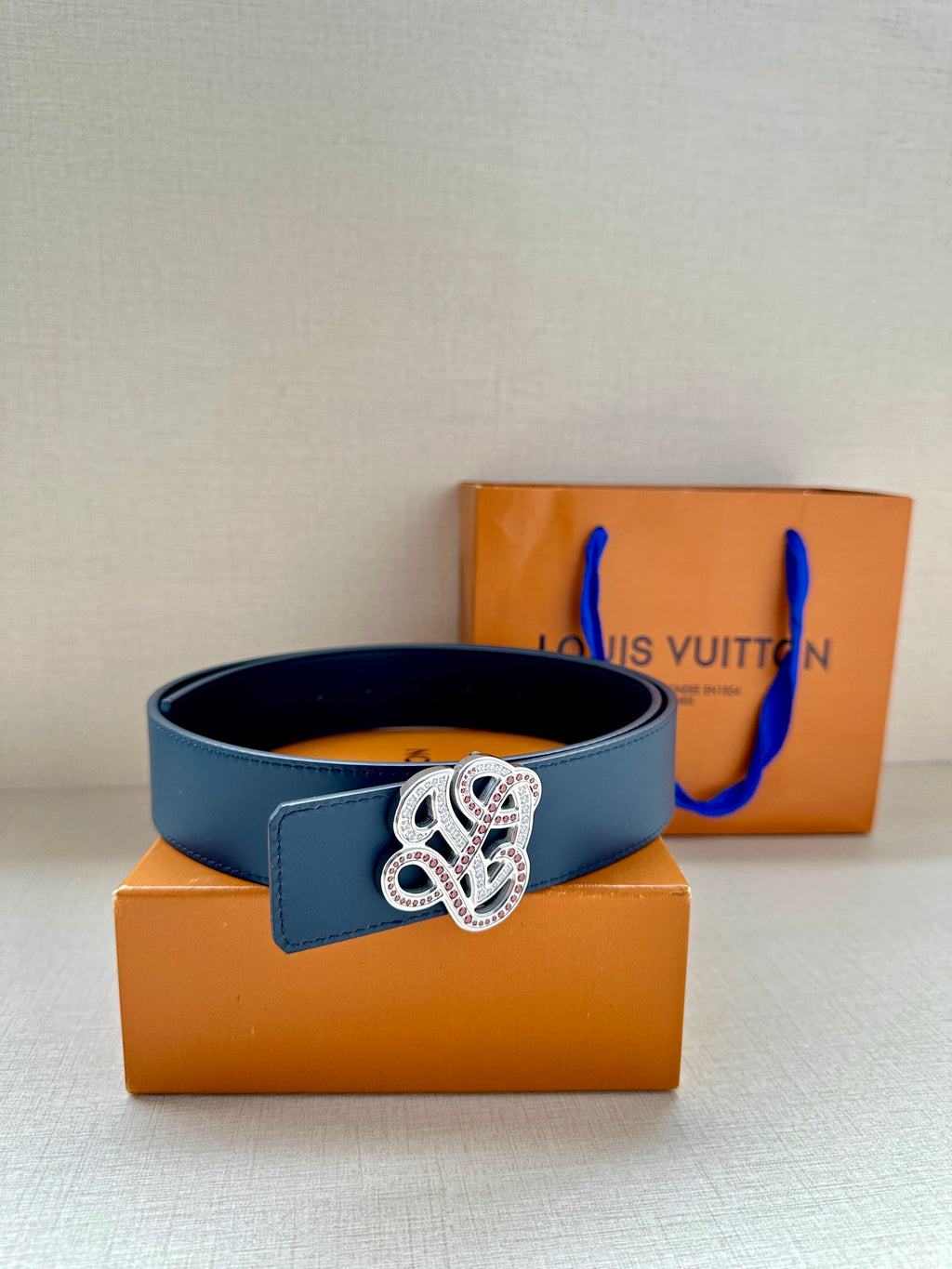 Dark blue leather belt with ornate buckle on top of orange gift box