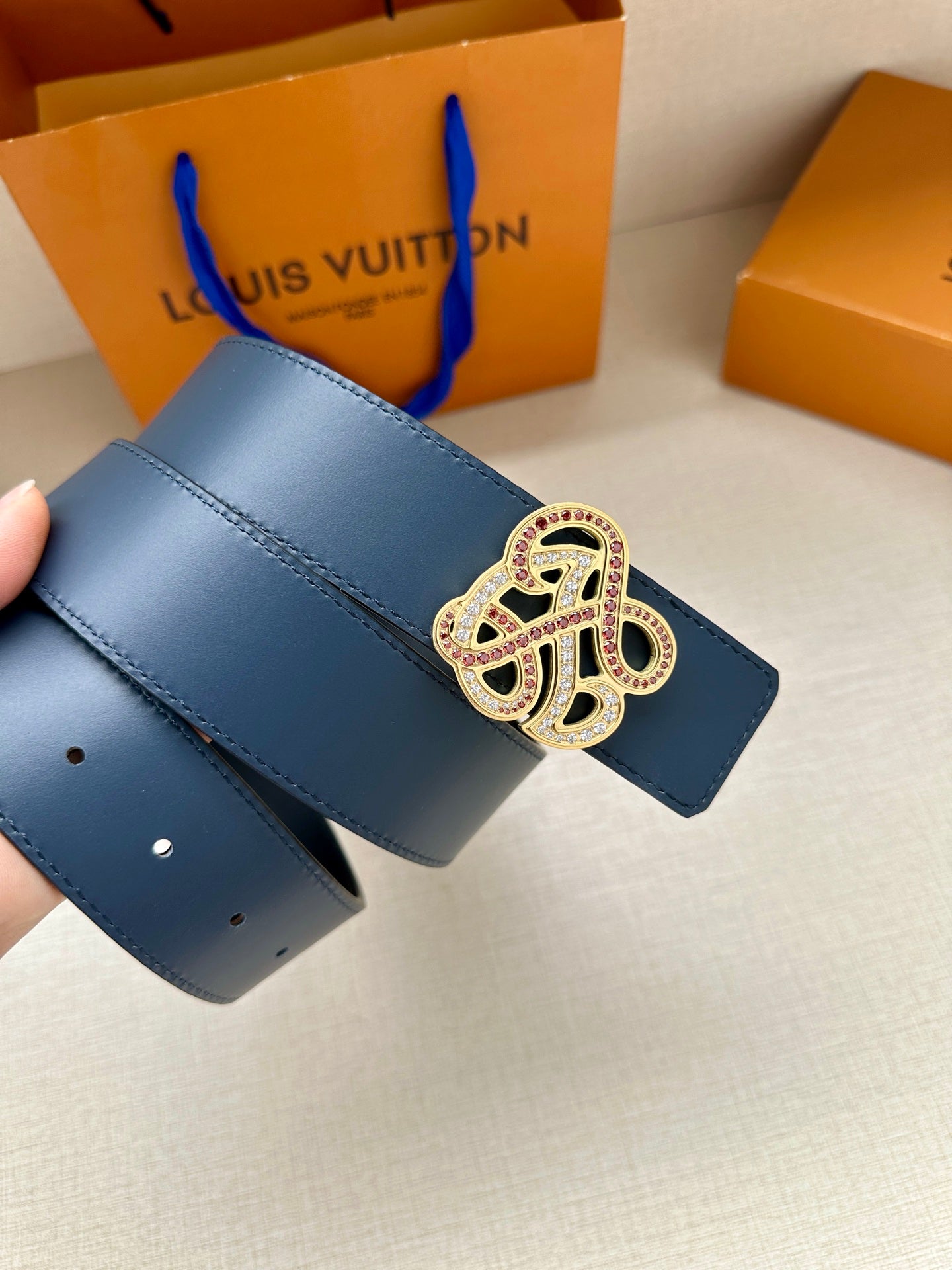 Dark blue leather belt strap held up with jeweled logo buckle