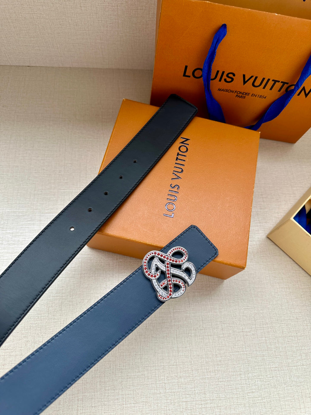 Dark blue leather belt with perforated strap and jeweled logo buckle