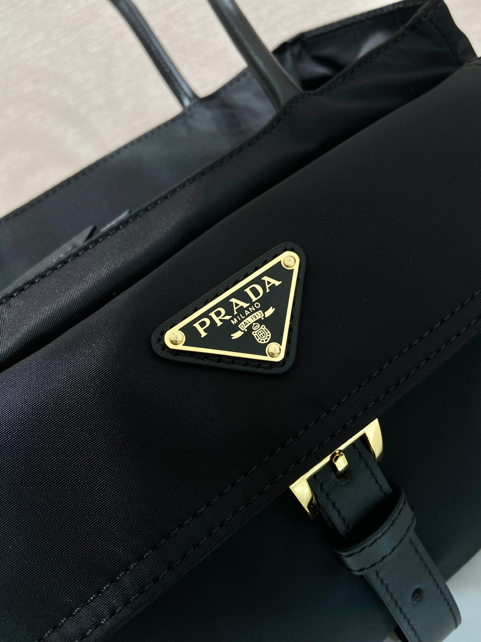 Prada black bag front flap with triangle logo plaque and gold buckle hardware