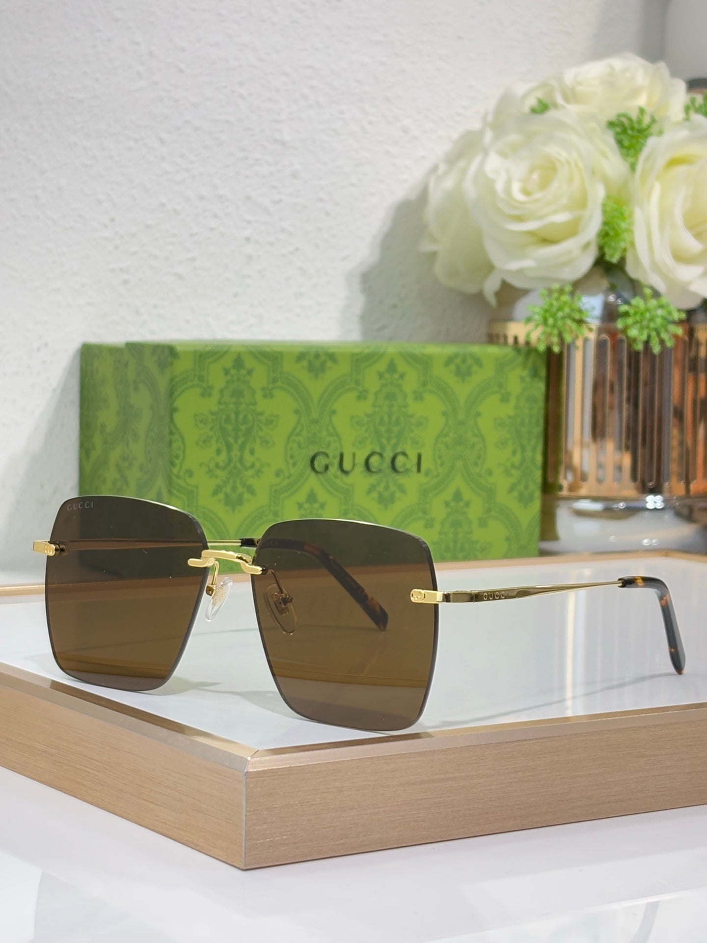 Gucci sunglasses with gold-tone frame and dark square lenses on display, front view.