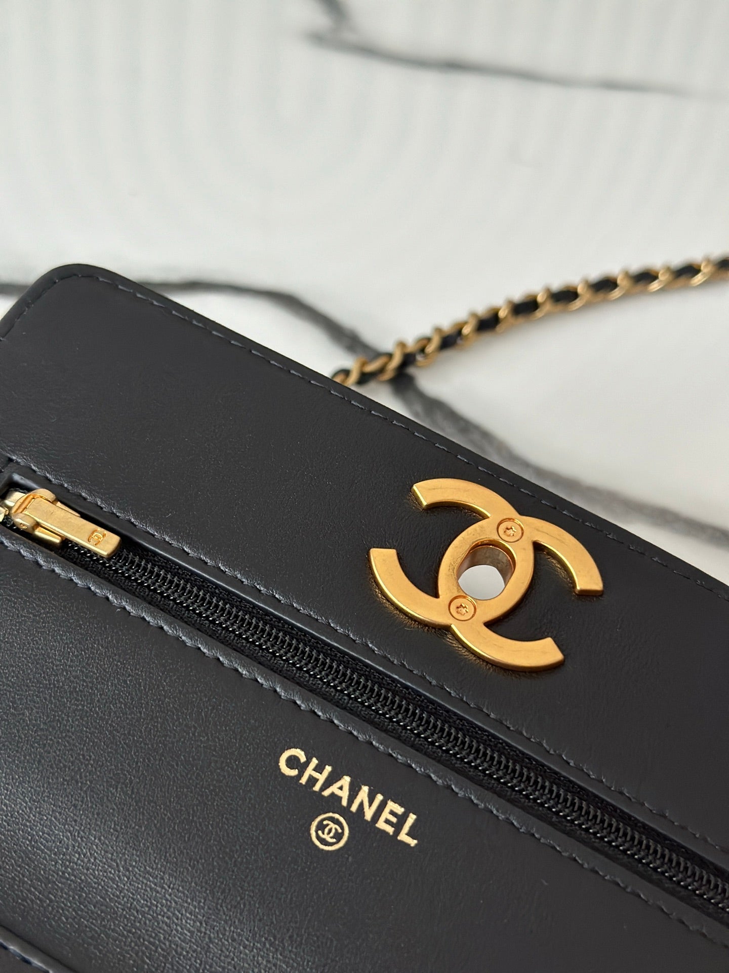 Close-up of Chanel black bag zipper with gold-tone CC logo on front pocket