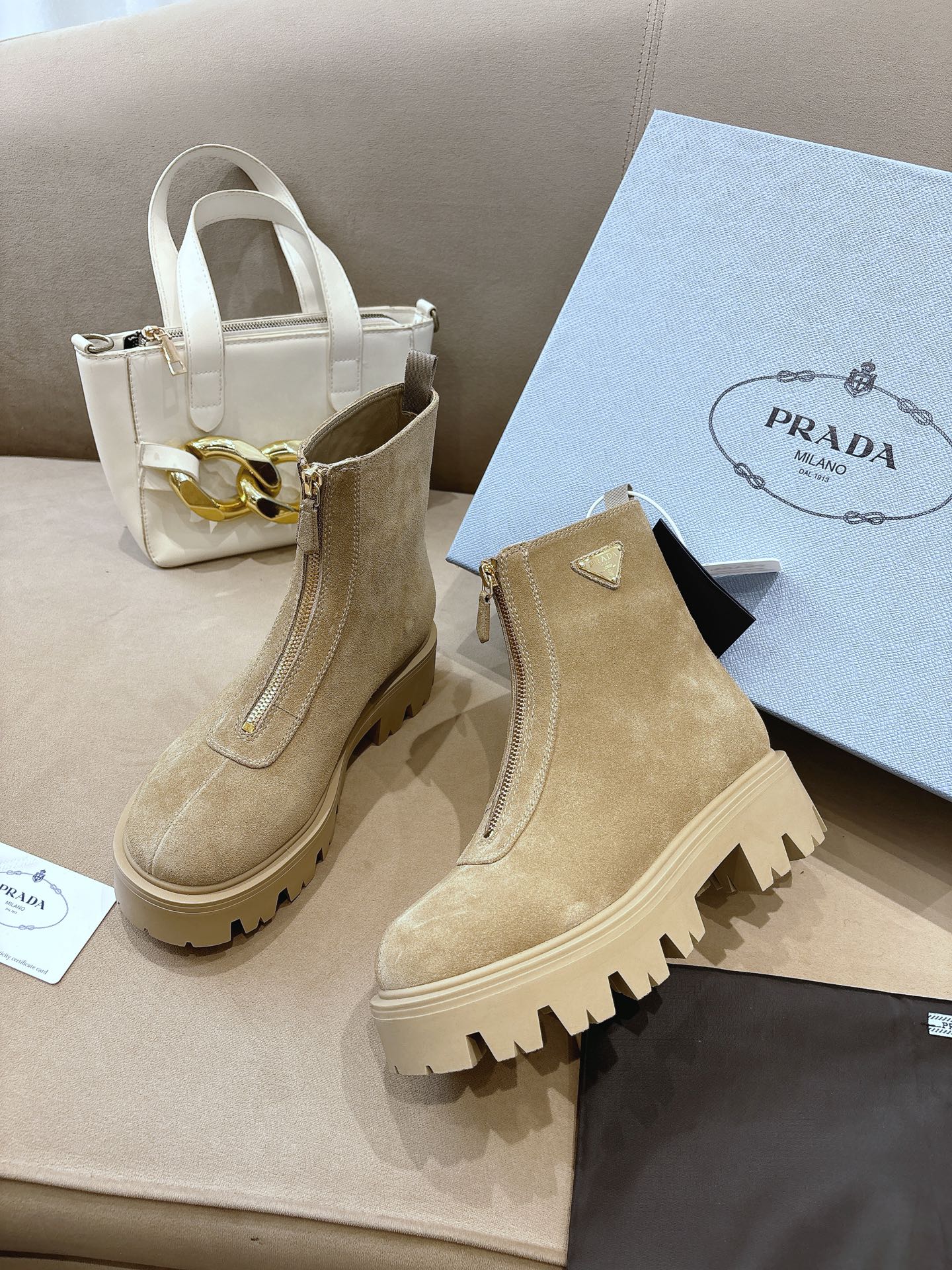 Beige suede Chelsea boots with triangular logo patch, side elastic, and chunky lug sole