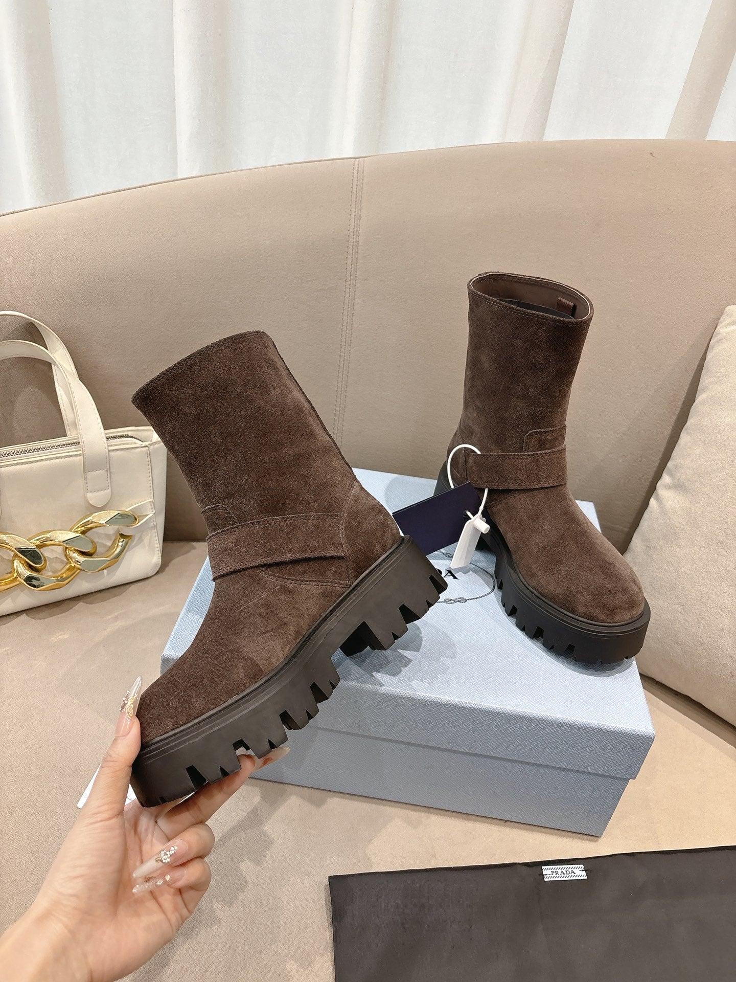 Brown suede ankle boots with strap buckle and thick lug sole, held up
