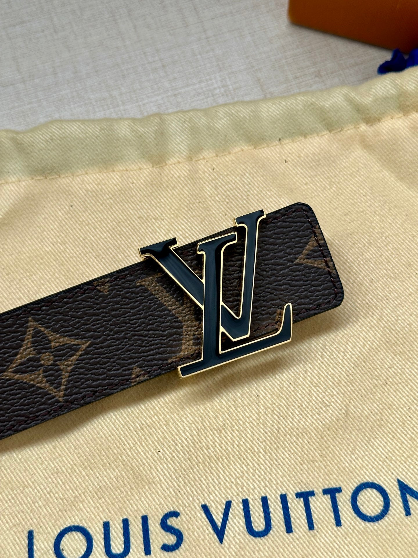 LV belt buckle on dark monogram canvas strap with gold-tone hardware and black leather.