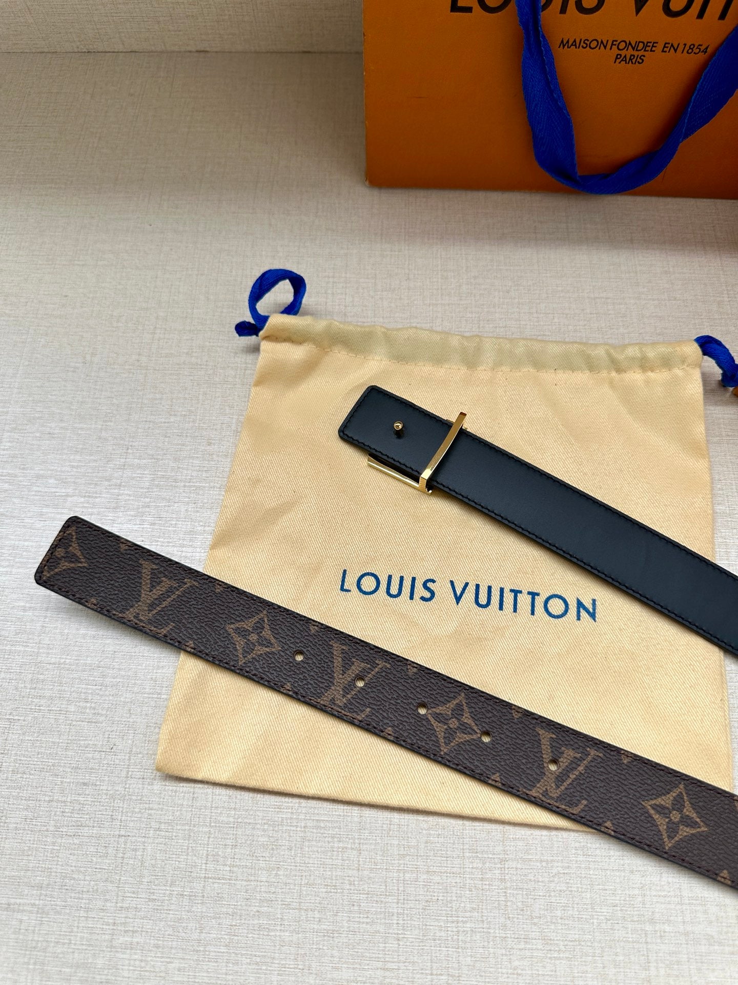 Monogram belt on cream drawstring bag, dark canvas strap with gold-tone LV buckle.