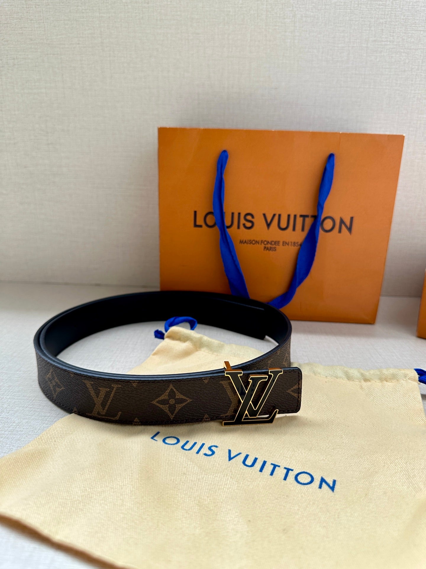 Monogram belt on cream dust cloth, dark canvas strap with gold-tone LV buckle.