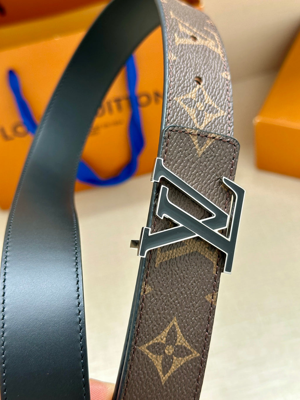 Close-up belt buckle: gold-tone LV on dark monogram canvas strap with black edge trim.