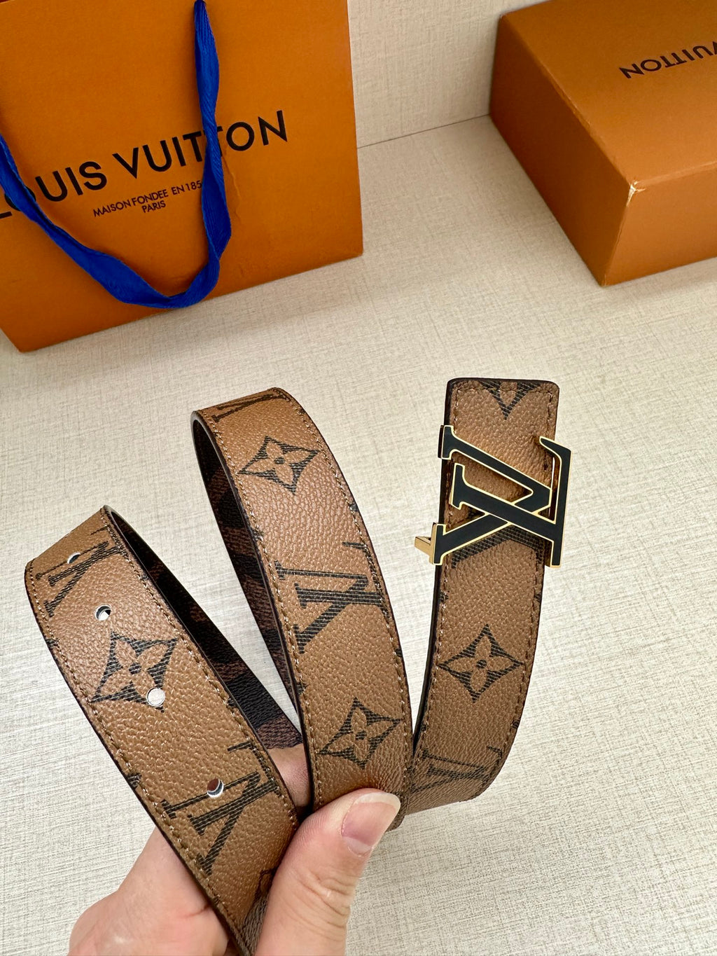 Louis Vuitton monogram belt strap held in hand with gold-tone LV buckle