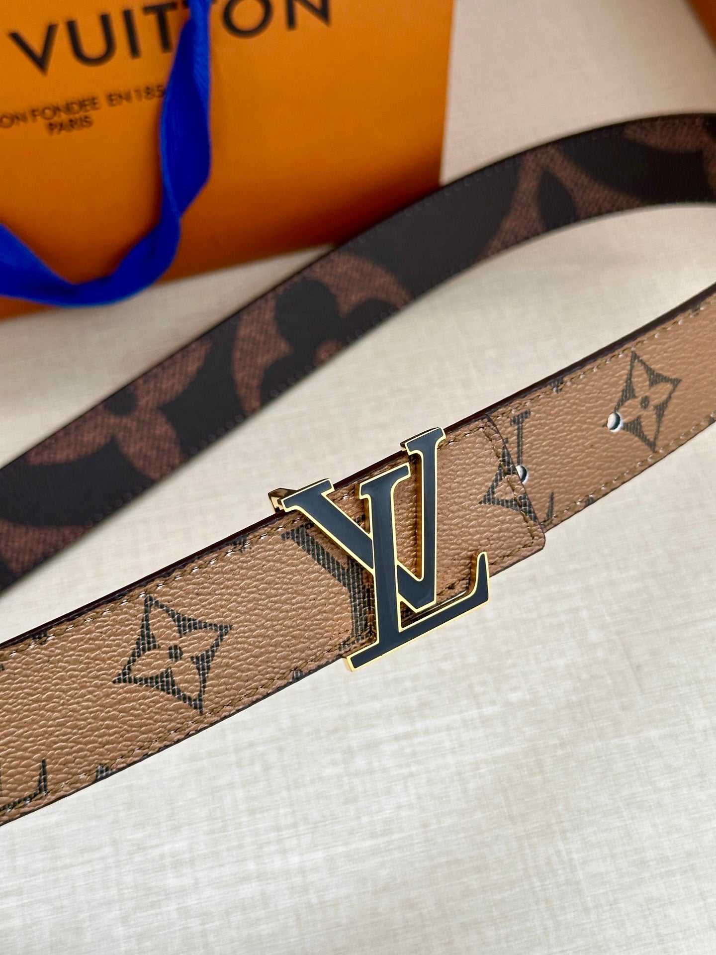 Louis Vuitton monogram belt buckle close-up with gold-tone LV and blue enamel