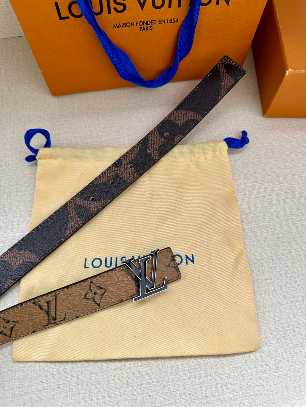 Louis Vuitton monogram belt strap with gold-tone LV buckle on cream pouch