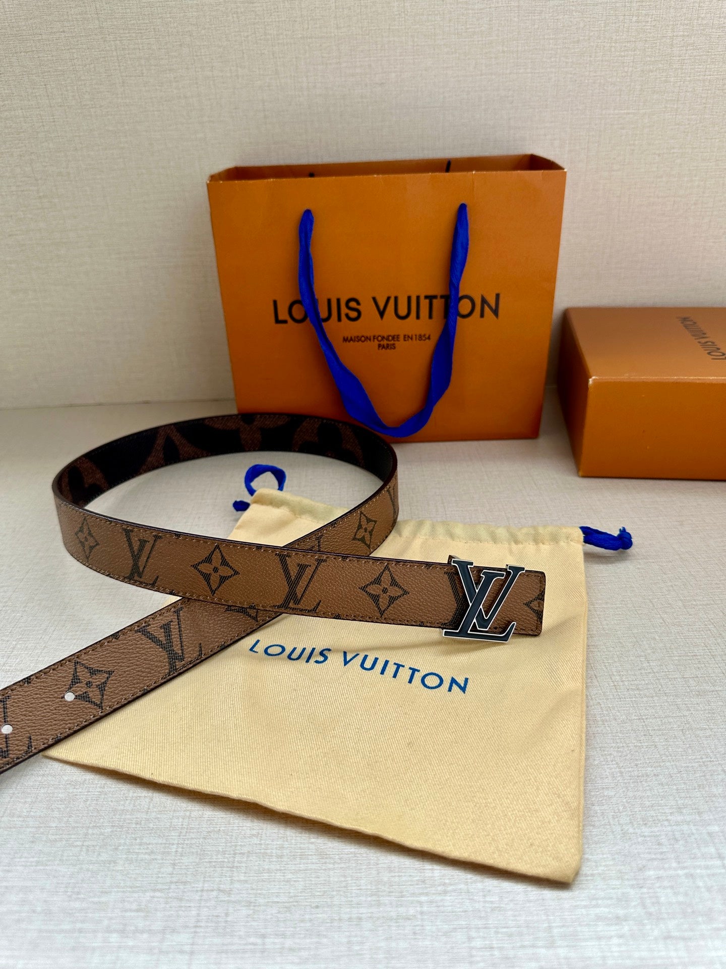 Louis Vuitton monogram belt with gold-tone LV buckle on cream dust bag