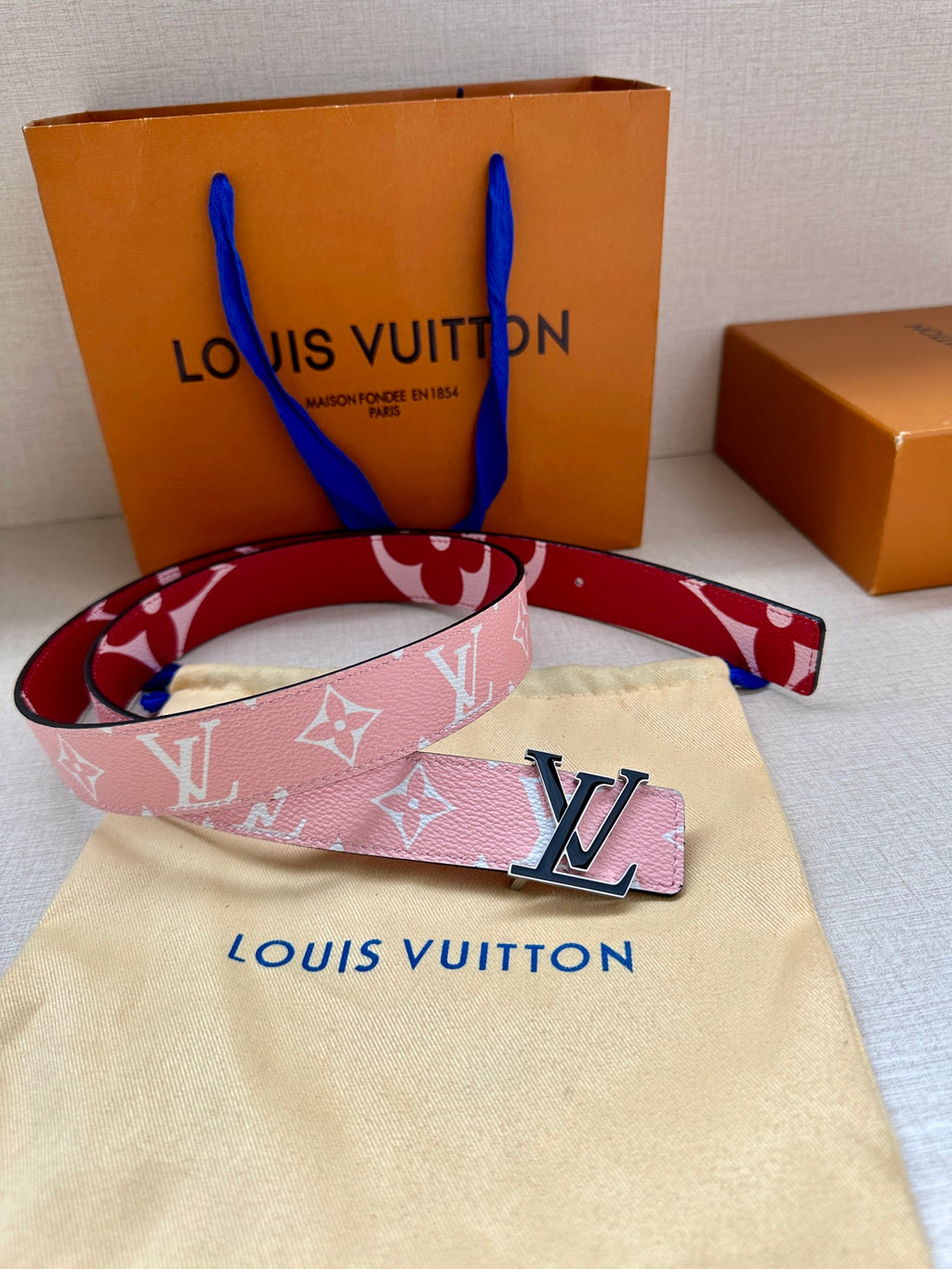 Pink monogram belt with silver LV buckle on beige dust bag