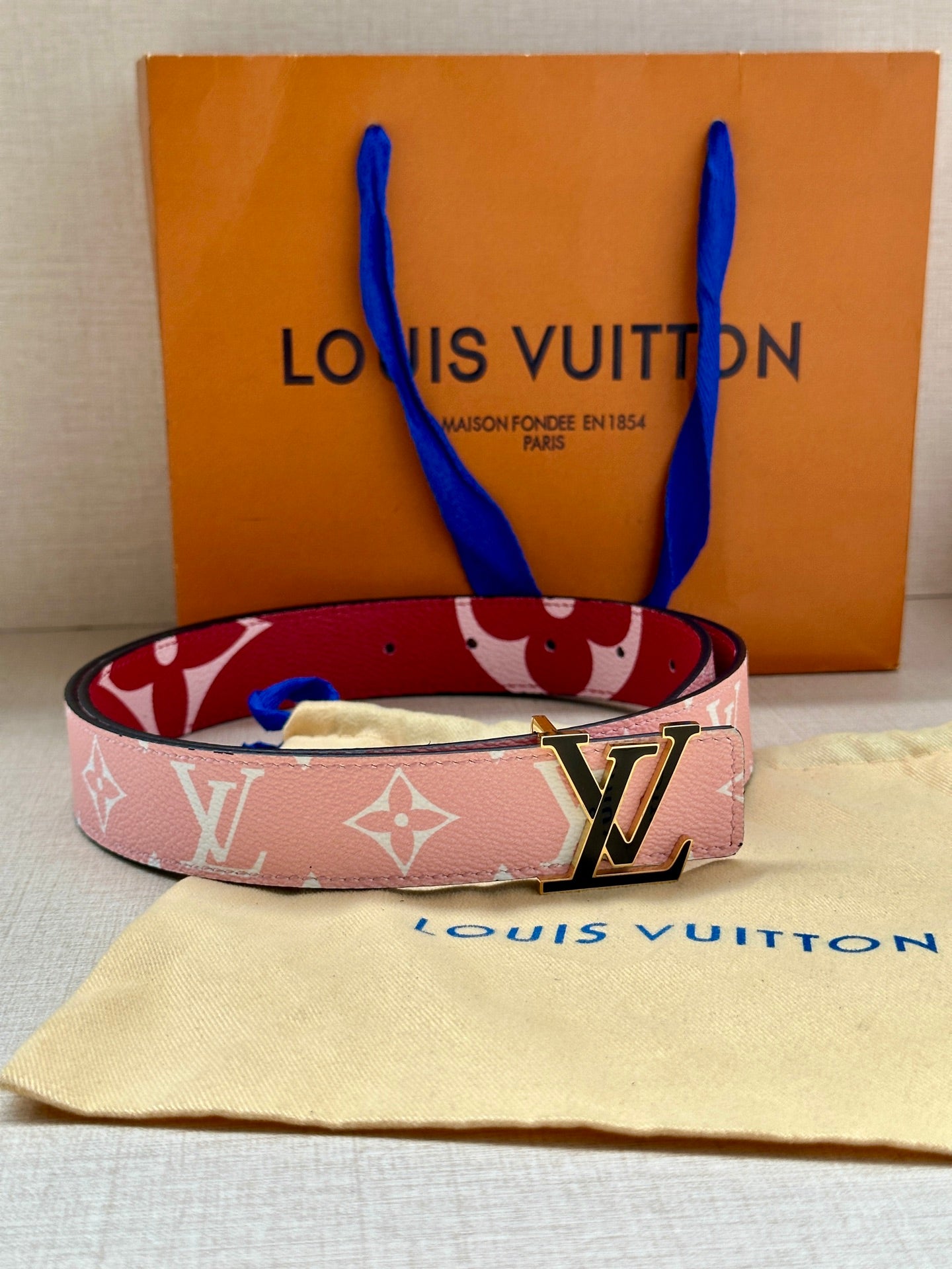 Pink monogram belt with silver LV buckle resting on dust bag