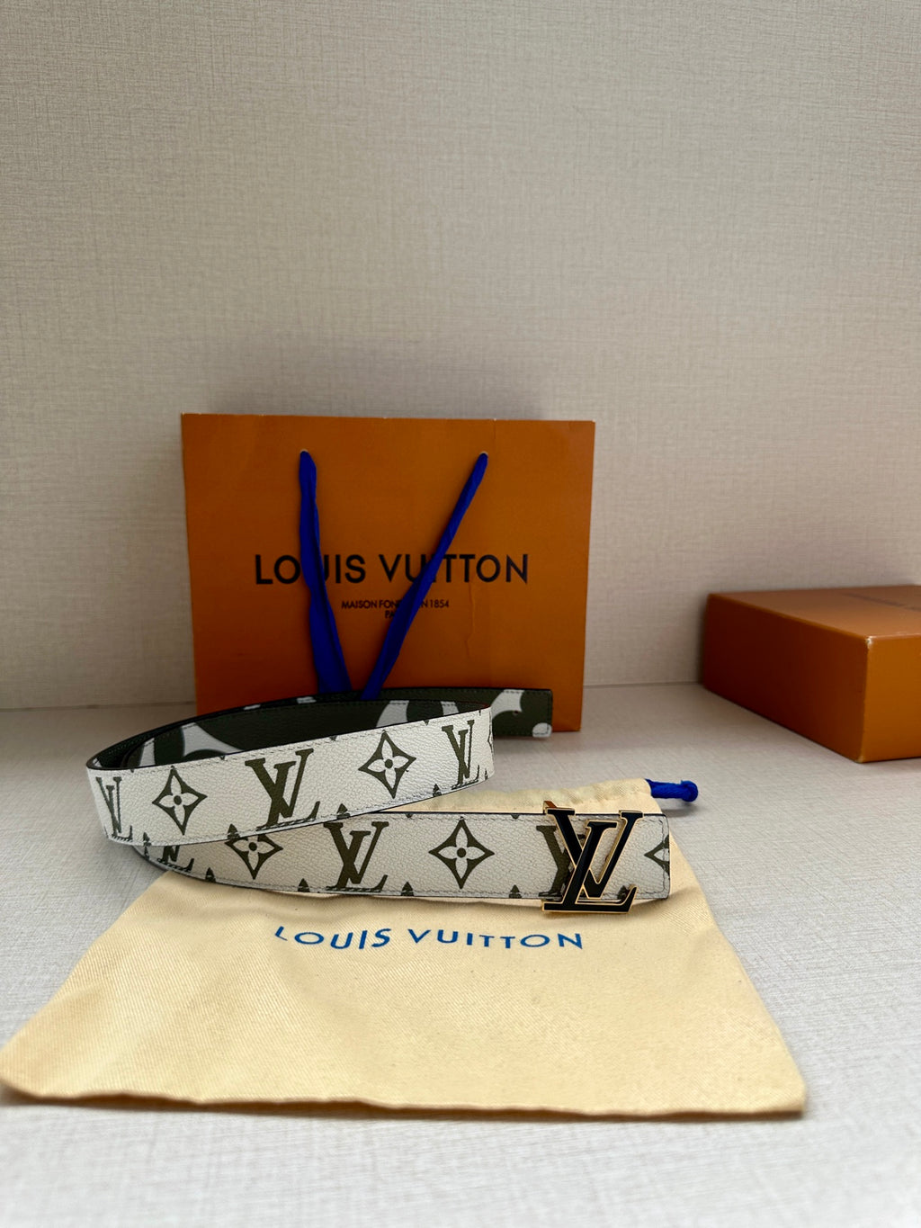 Louis Vuitton belt laid flat: white monogram pattern, dark green trim, silver LV buckle