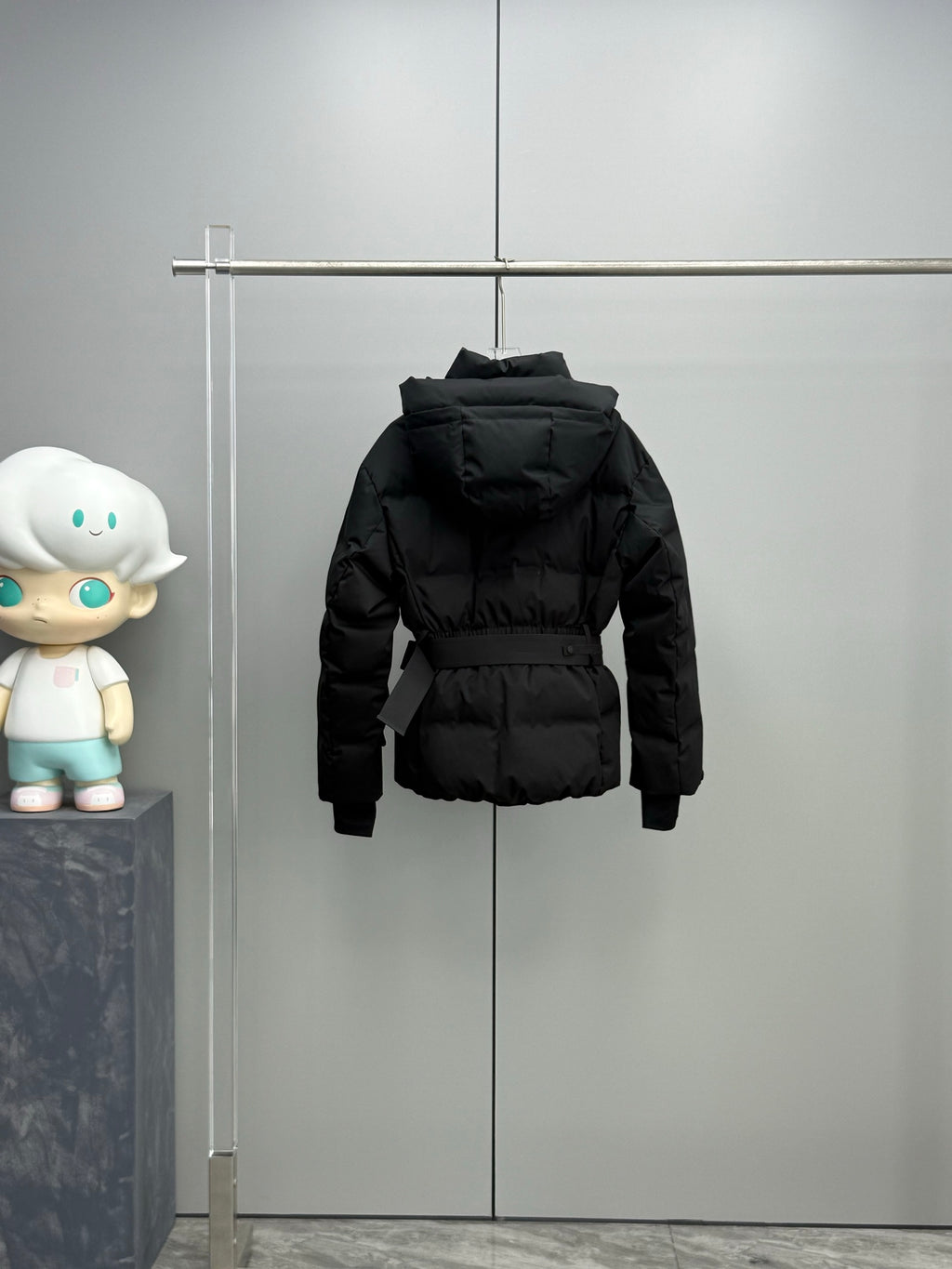 Black hooded long puffer jacket hanging, with front zipper and waist belt