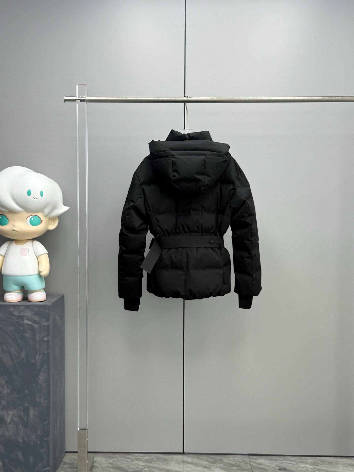 Black hooded long puffer jacket hanging, with front zipper and waist belt