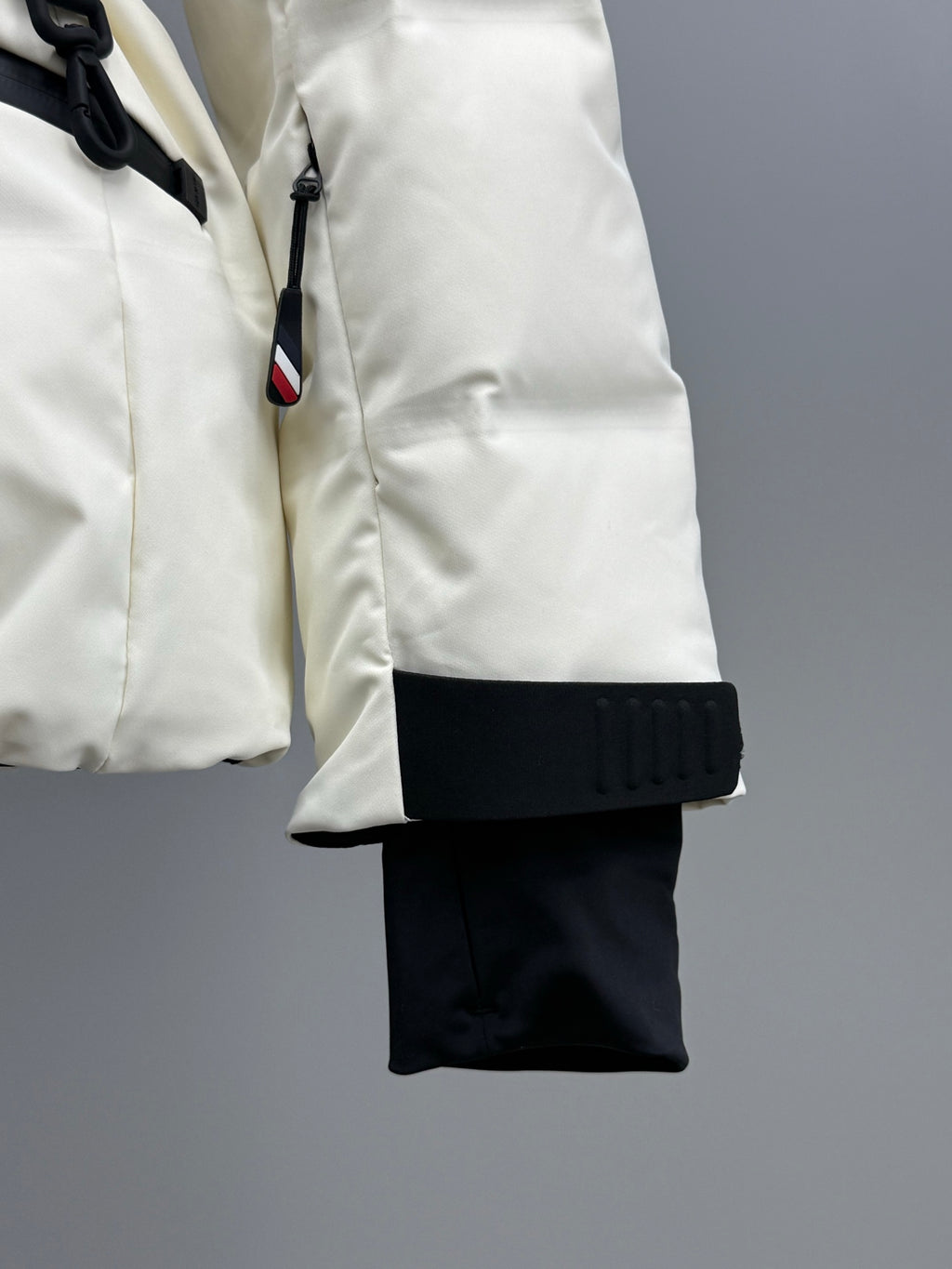 White puffer jacket with hood drawstring, black cuff detail, and hanging strap