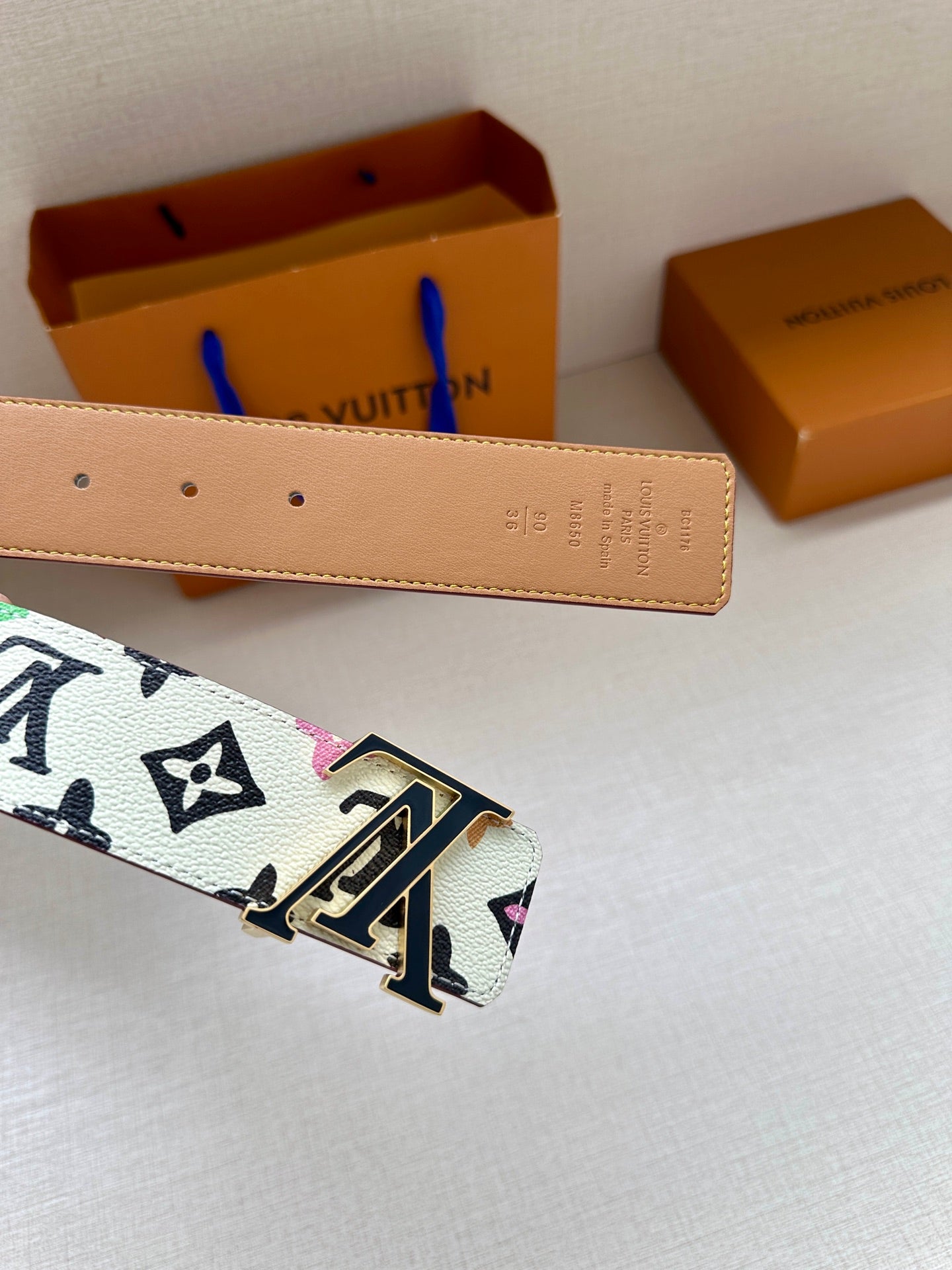 Leather belt with tan back and gold LV buckle, monogram strap visible