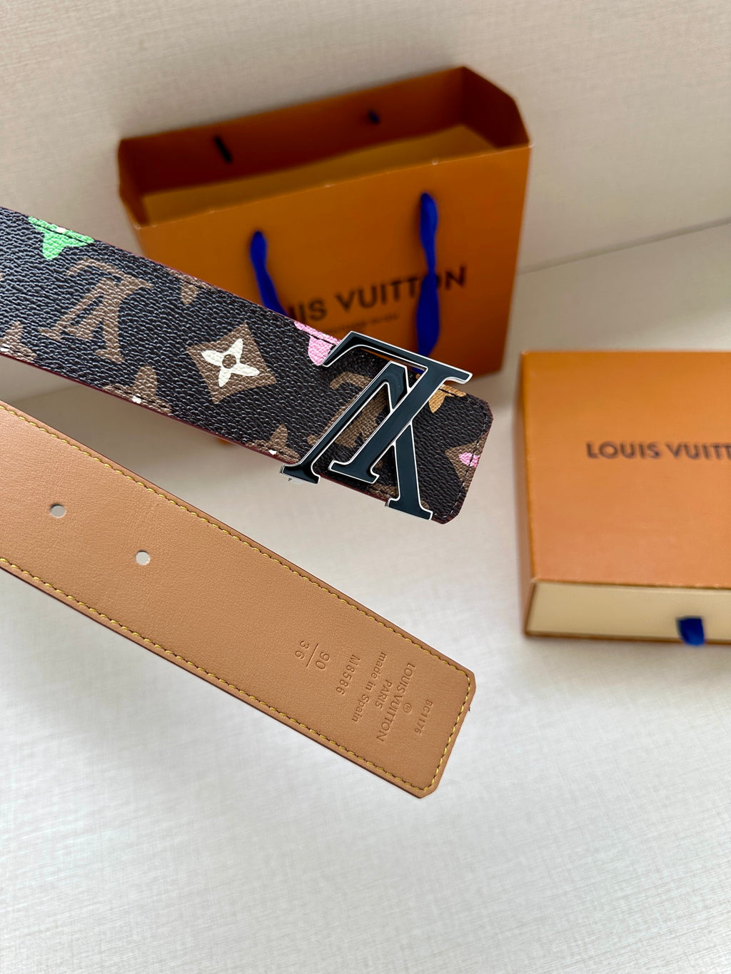 Tan leather belt strap with punch holes, showing navy monogram and silver buckle