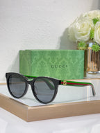 Gucci sunglasses with black round frames and dark lenses, green temple with red stripe.