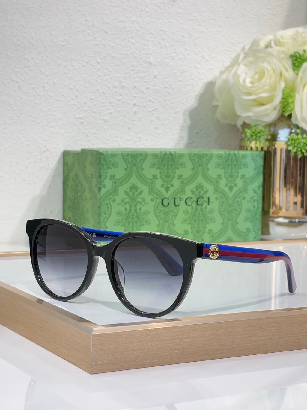 Gucci round sunglasses with black frames and dark lenses, blue-to-green temple accents.