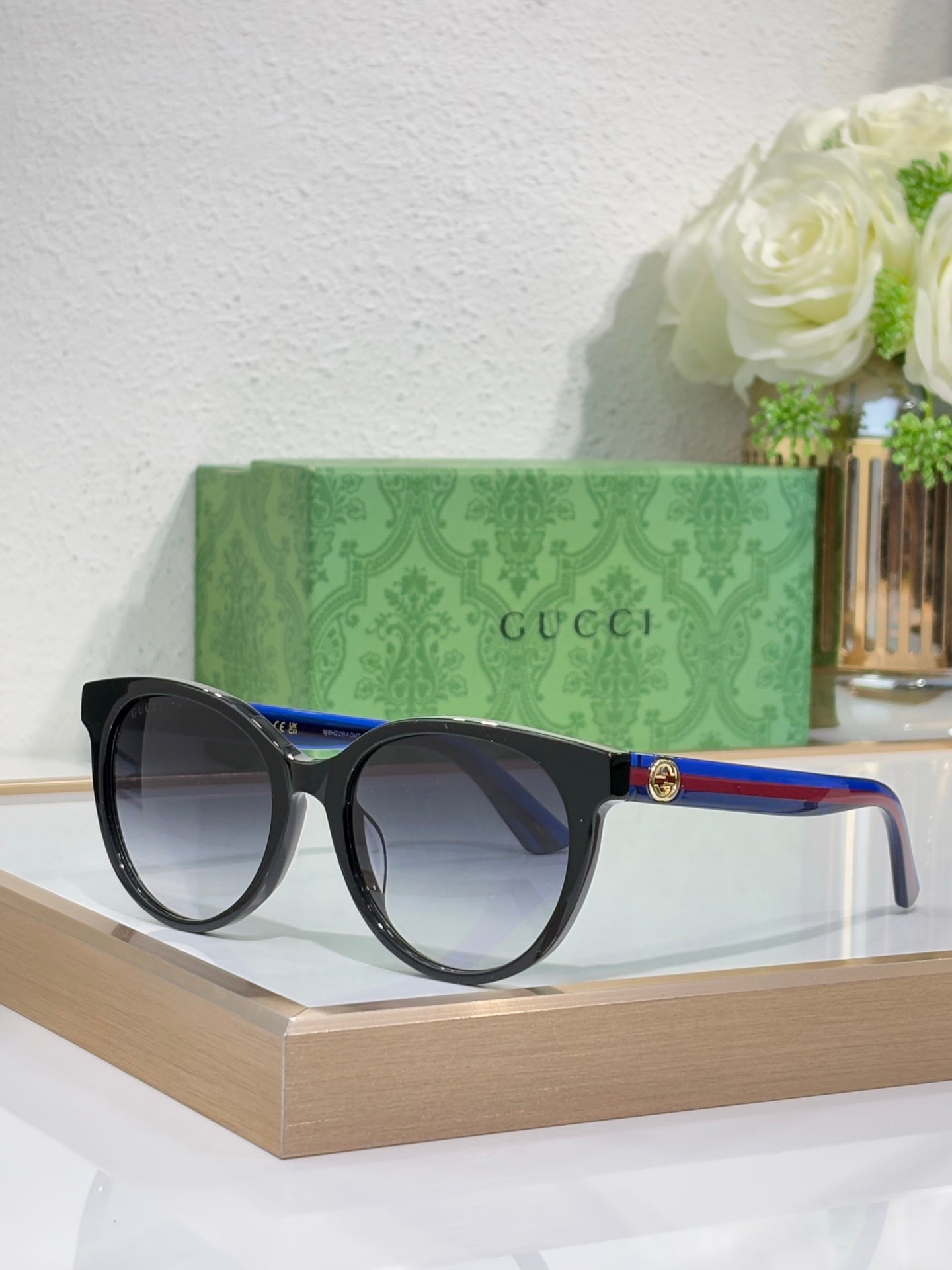 Gucci round sunglasses with black frames and dark lenses, blue-to-green temple accents.