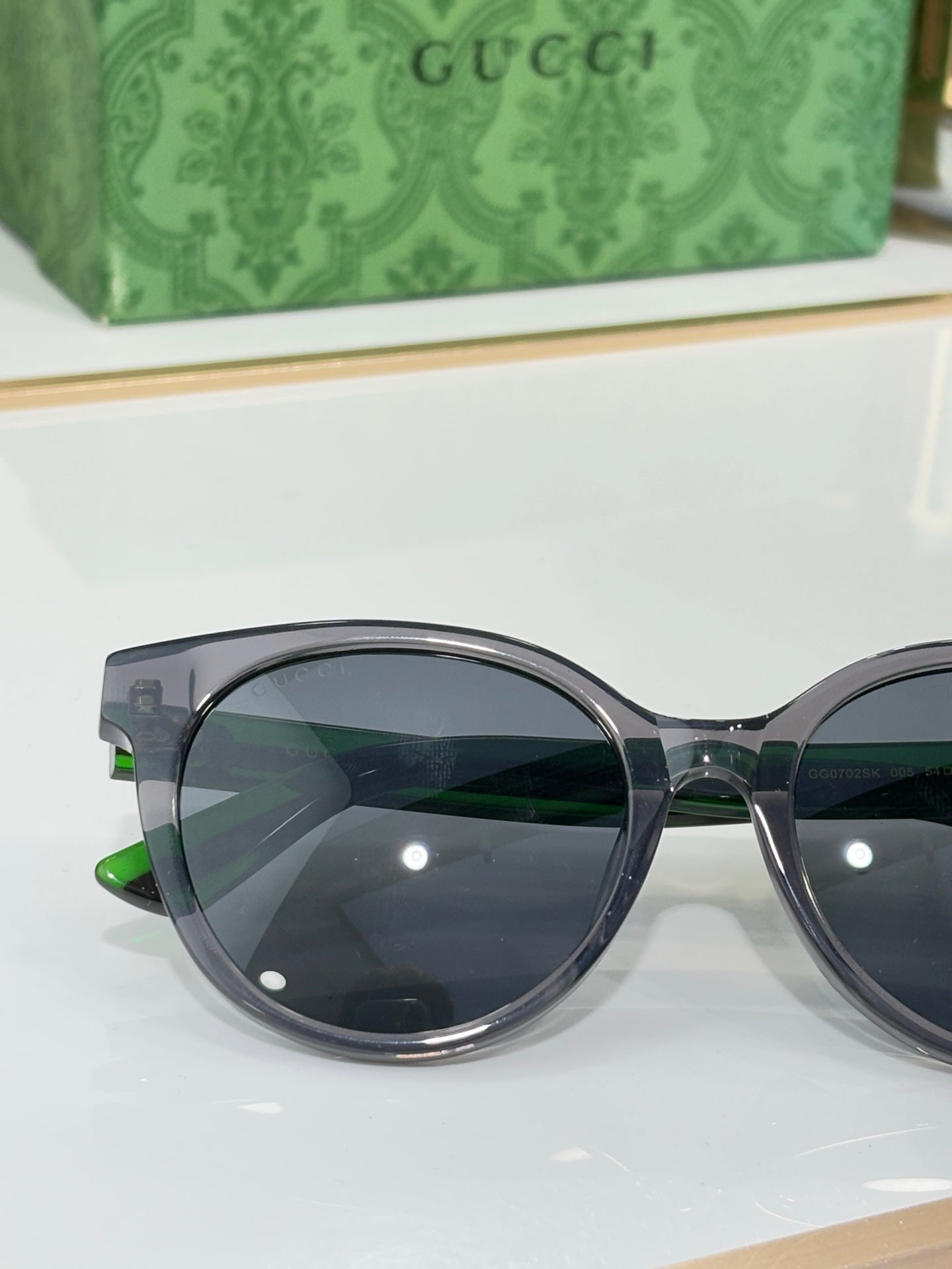 Gucci close-up sunglasses: black round frame, dark lenses, green temple accent line.