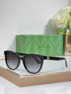 Gucci sunglasses with black round frames, green-and-red temple accents, gold logo.